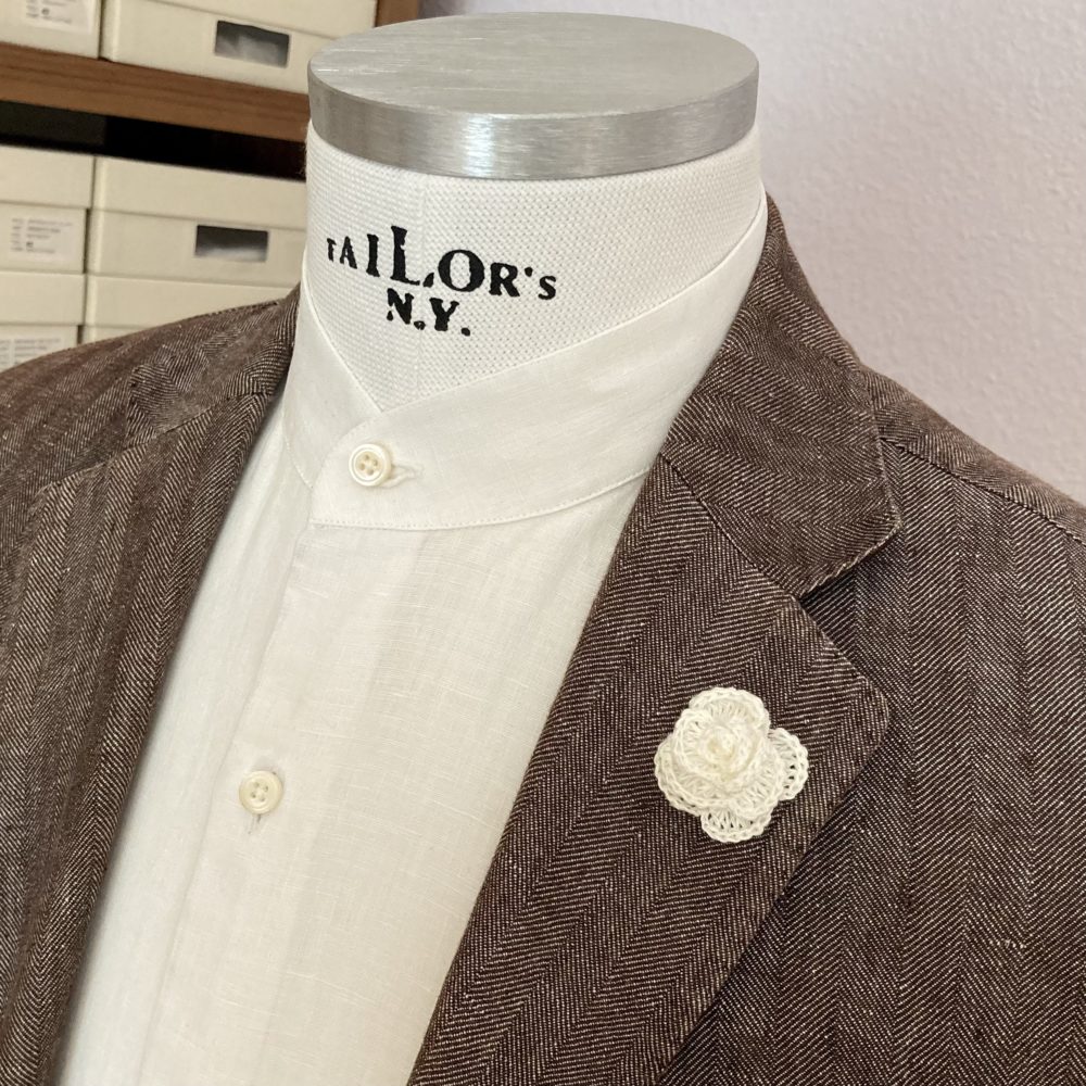 Bild zeigt weisses Stehkragen Hemd aus Leinen unter braunem Jacket mit einer Ansteckblume